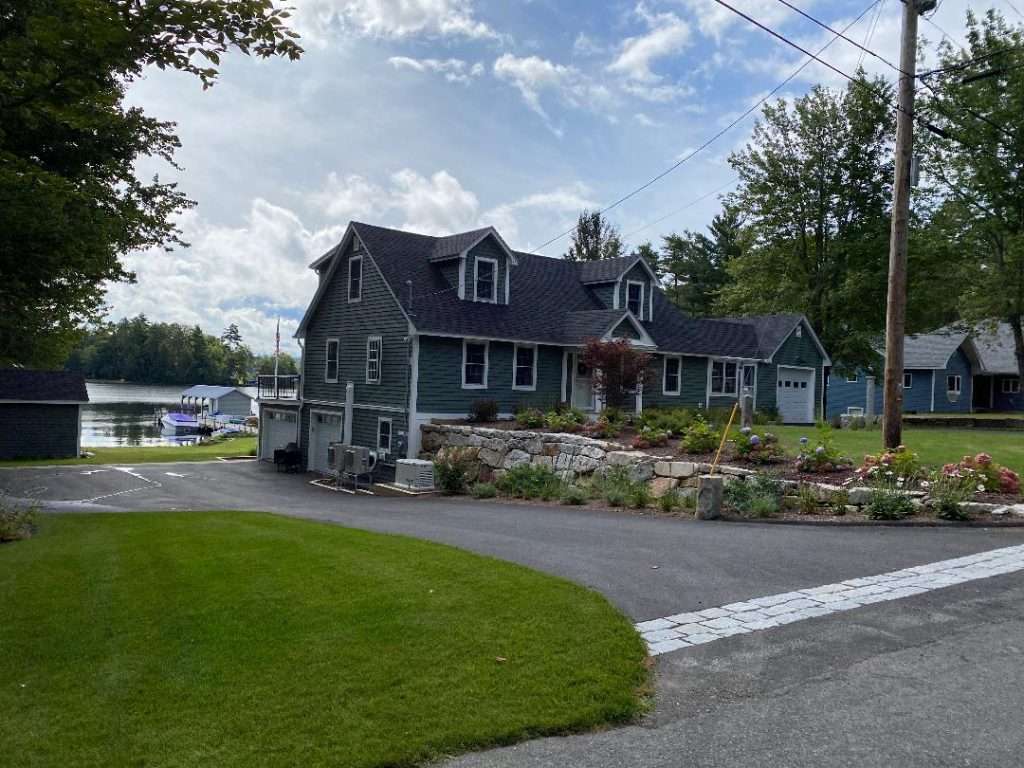 Natural stone retaining wall and complete landscape installation featuring flowering garden beds, ornamental plantings, granite curb detail, and lakeside home landscaping in New Hampshire