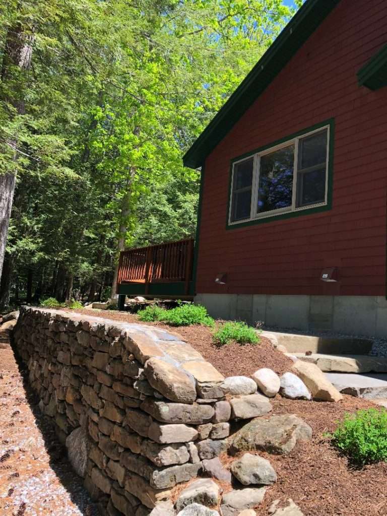 Natural stone retaining wall and hillside landscape installation for a woodland New Hampshire home by Landscapes by Tom