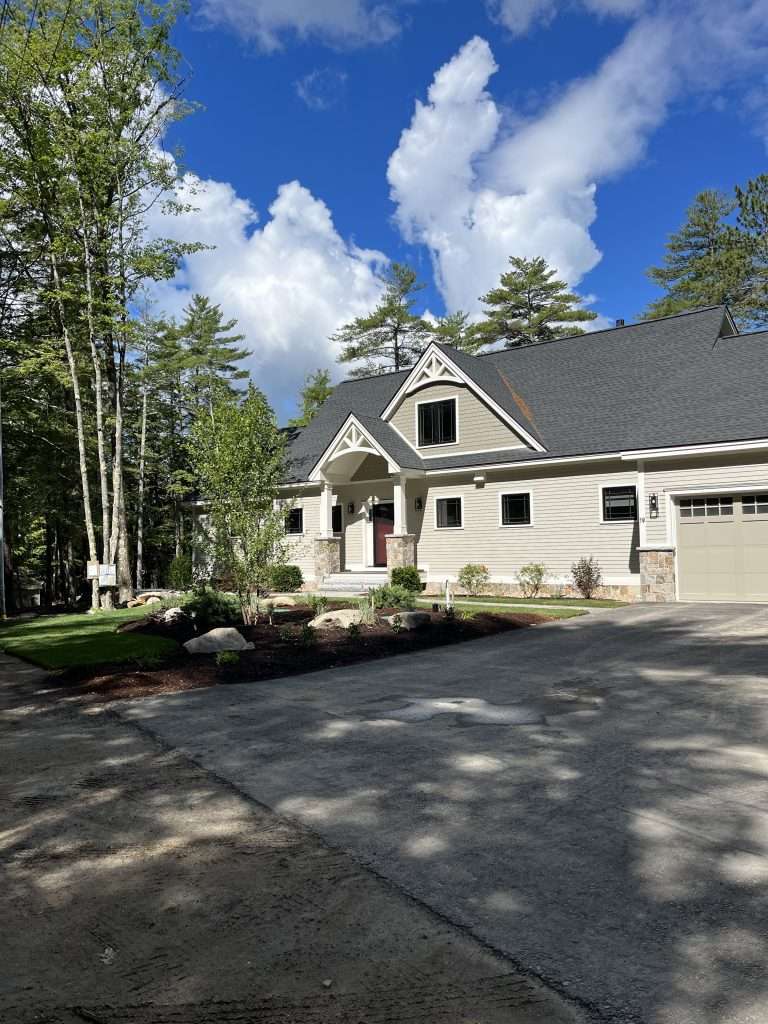 Custom lakefront outdoor living space featuring a multi-level paver patio, built-in fire pit, natural stone sitting walls, granite steps, landscape lighting, and professionally designed planting beds with stunning waterfront views in New Hampshire
