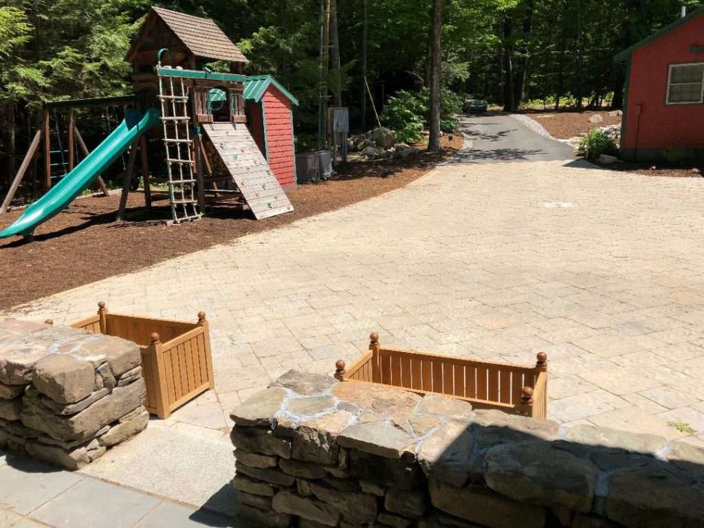 Large custom paver courtyard and driveway installation with natural stone walls by Landscapes by Tom in New Hampshire