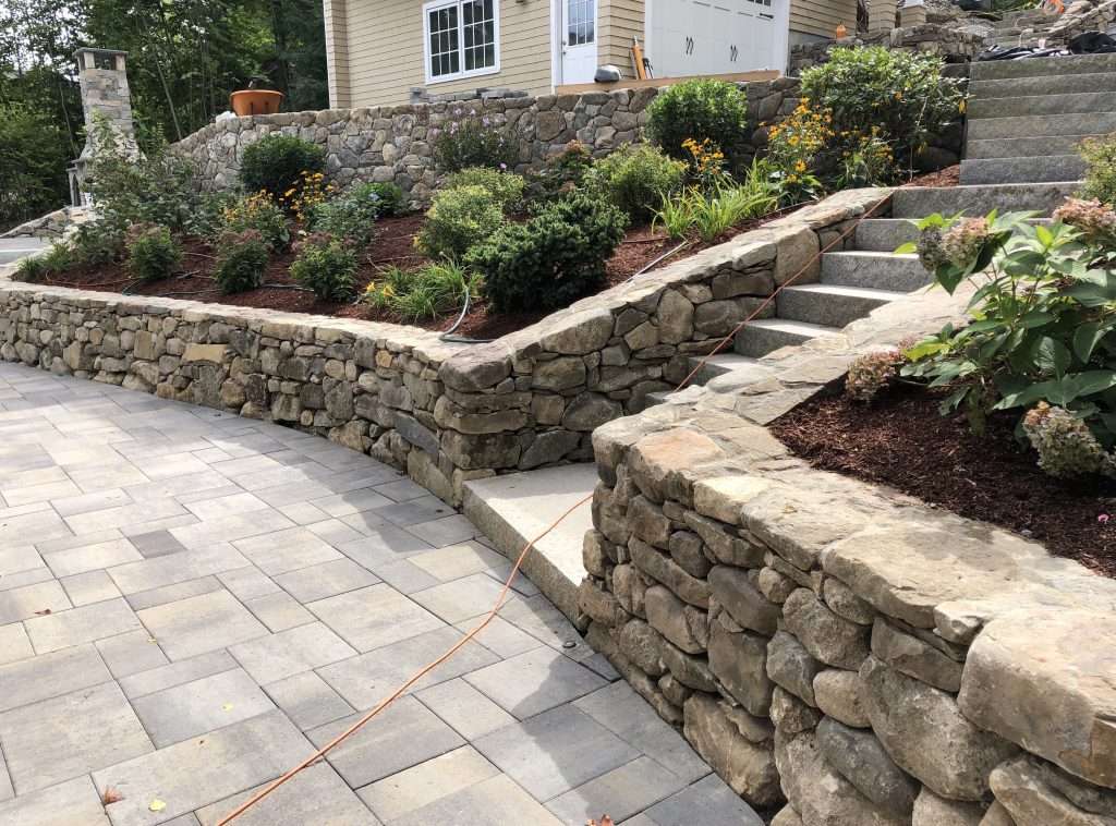 Completed retaining wall, paver patio, and landscape planting installation for a New Hampshire home by Landscapes by Tom