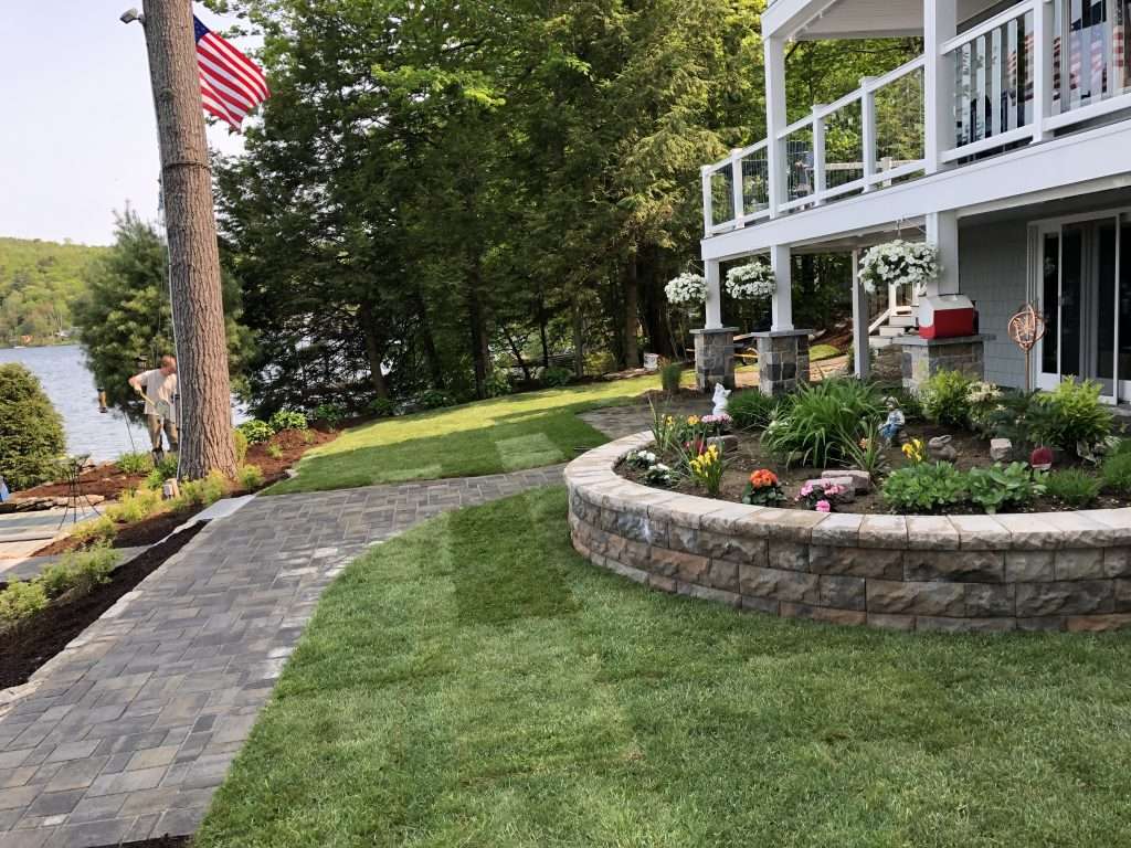 Curved retaining wall, custom paver walkway, and lakeside landscape installation with colorful perennial gardens and fresh lawn renovation in New Hampshire