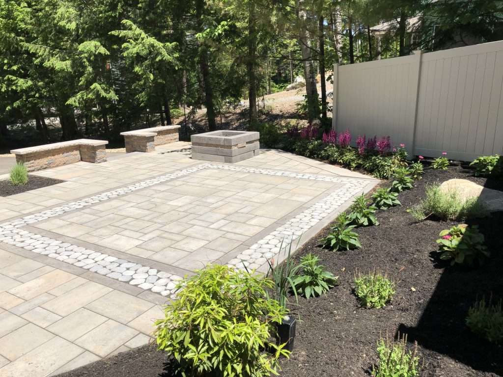 Custom paver patio with decorative river rock inlay, modern fire pit, geometric hardscape design, and landscaped garden beds for a stylish backyard outdoor living space 3