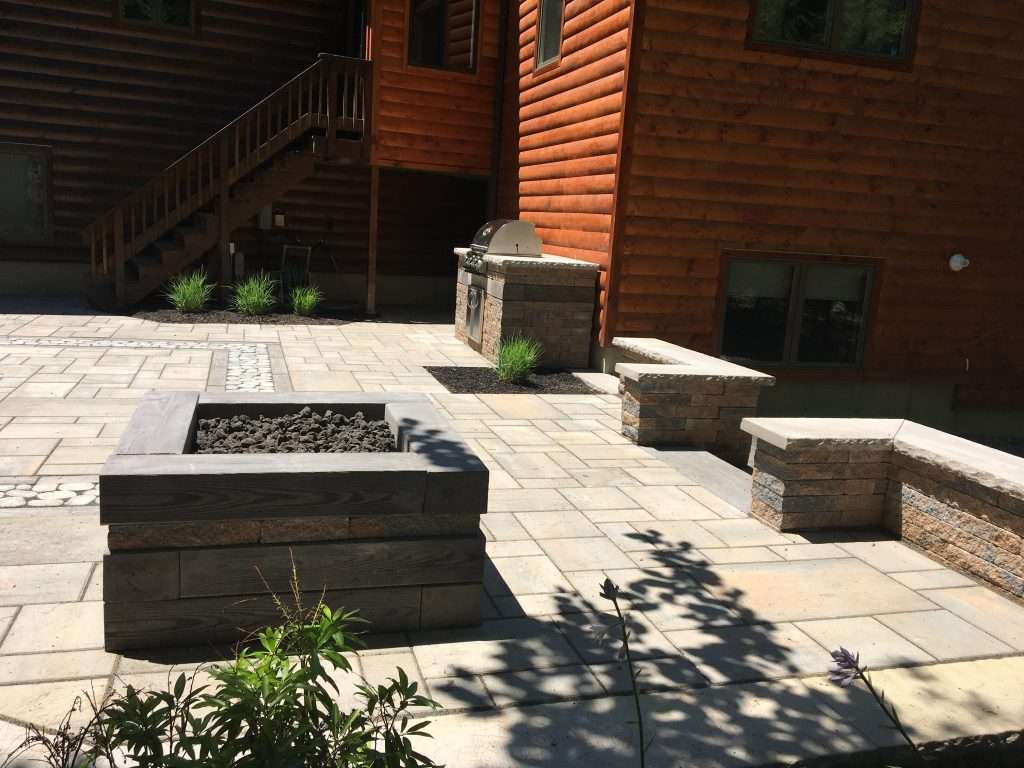 Luxury backyard patio with custom paver installation, modern fire pit, built-in outdoor kitchen and grill station, seating walls, and decorative stone accents for a New Hampshire outdoor living space