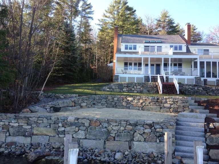 Retaining wall landscaping project featuring natural stone wall construction, erosion control solutions, terraced garden design, drainage improvements, and custom hardscape installation for a New Hampshire property by Landscapes by Tom