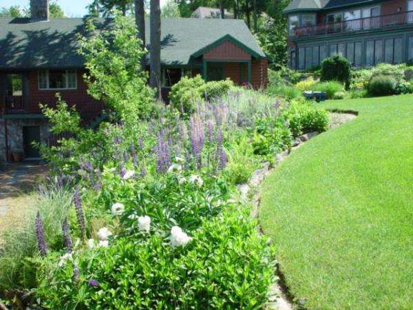 Charming garden house surrounded by colorful perennial flower beds, natural stone landscaping, and professionally designed cottage-style garden plantings in New Hampshire