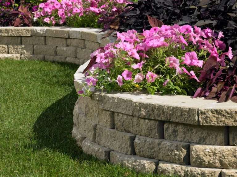 Natural stone retaining wall installation with terraced landscaping, decorative plantings, erosion control, and handcrafted hardscape design for a New Hampshire property by Landscapes by Tom