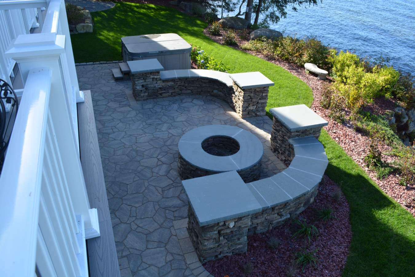 Custom outdoor living patio with curved stone seating walls, built-in fire pit, natural stone veneer, and lakeside entertaining space in New Hampshire